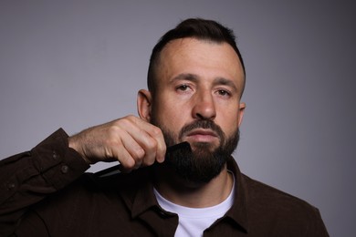 Photo of Handsome man combing beard on grey background