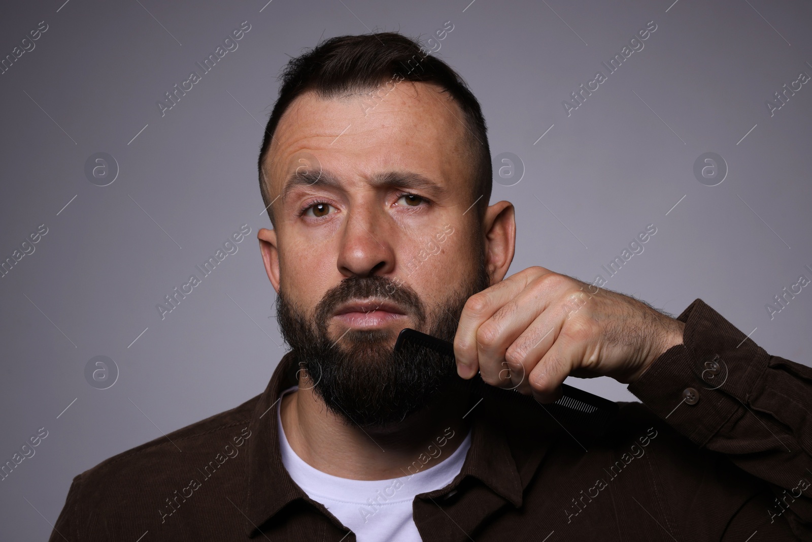 Photo of Handsome man combing beard on grey background