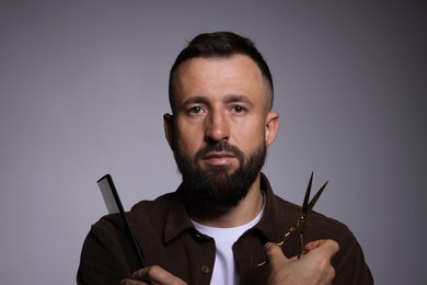 Photo of Bearded man holding comb and scissors on grey background