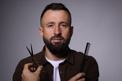 Photo of Bearded man holding comb and scissors on grey background