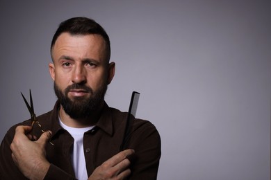 Photo of Bearded man holding comb and scissors on grey background, space for text