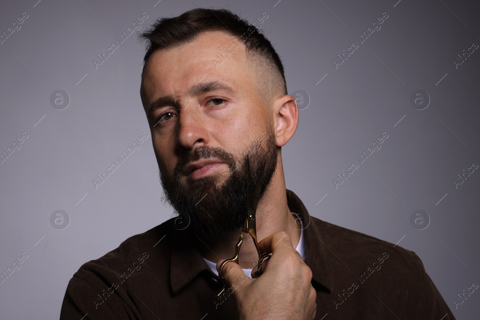 Photo of Man trimming beard with scissors on grey background