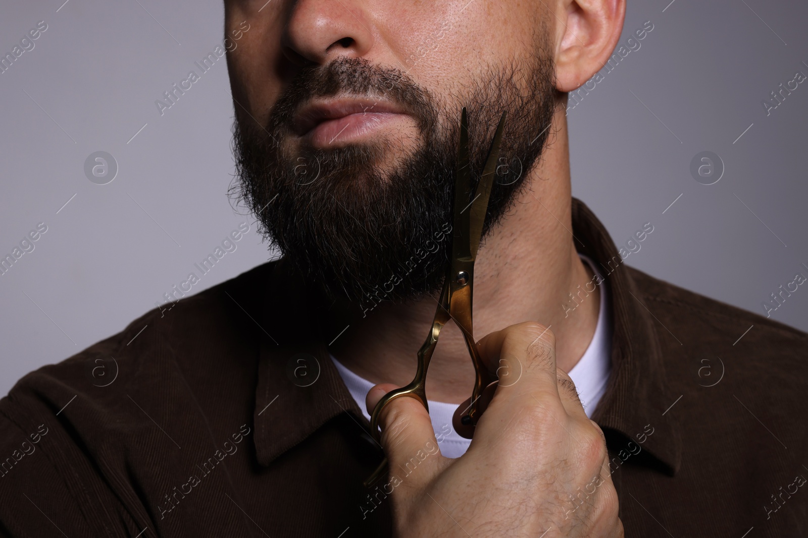 Photo of Man trimming beard with scissors on grey background, closeup