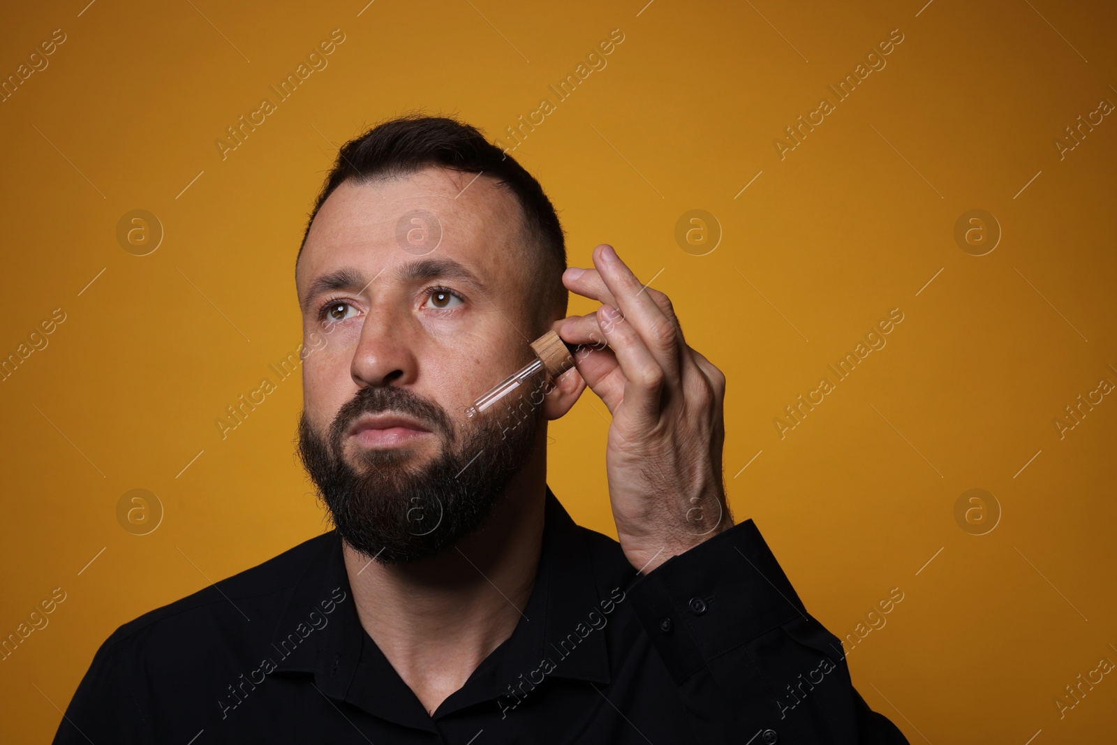 Photo of Man applying serum onto his beard on orange background