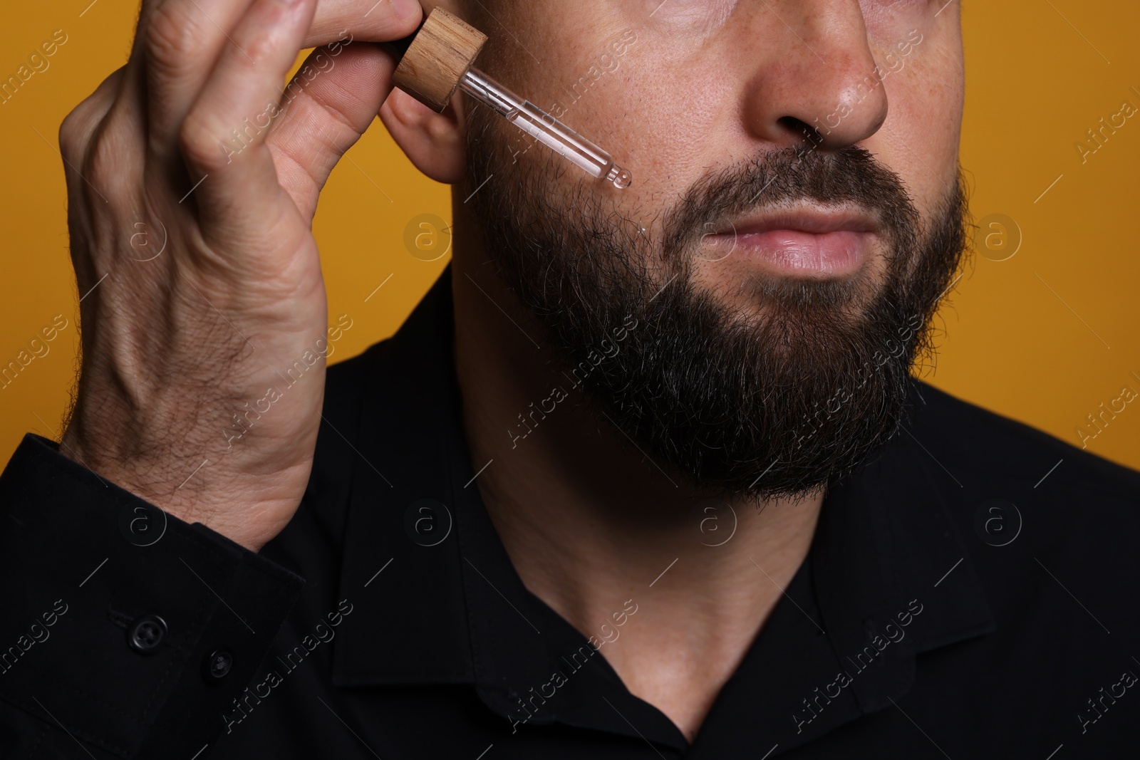 Photo of Man applying serum onto his beard on orange background, closeup