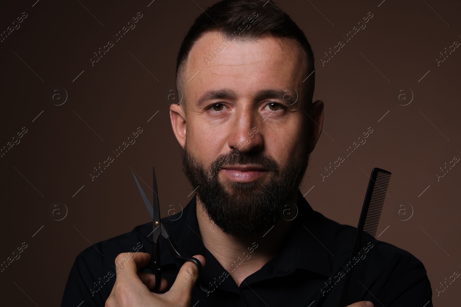 Photo of Bearded man holding comb and scissors on brown background