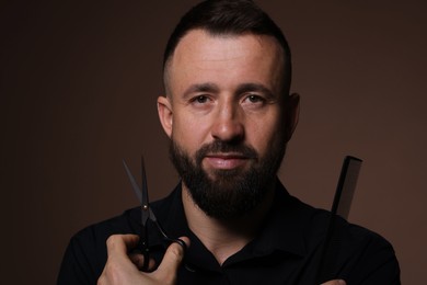 Photo of Bearded man holding comb and scissors on brown background