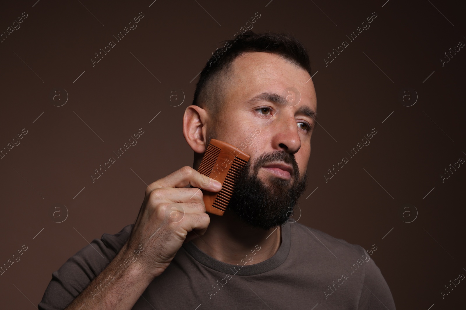 Photo of Handsome man combing beard on brown background