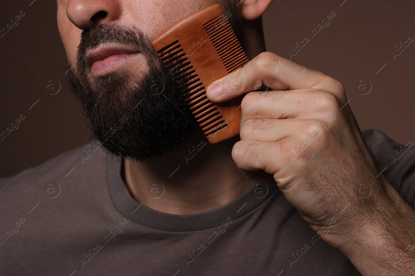 Photo of Man combing beard on brown background, closeup