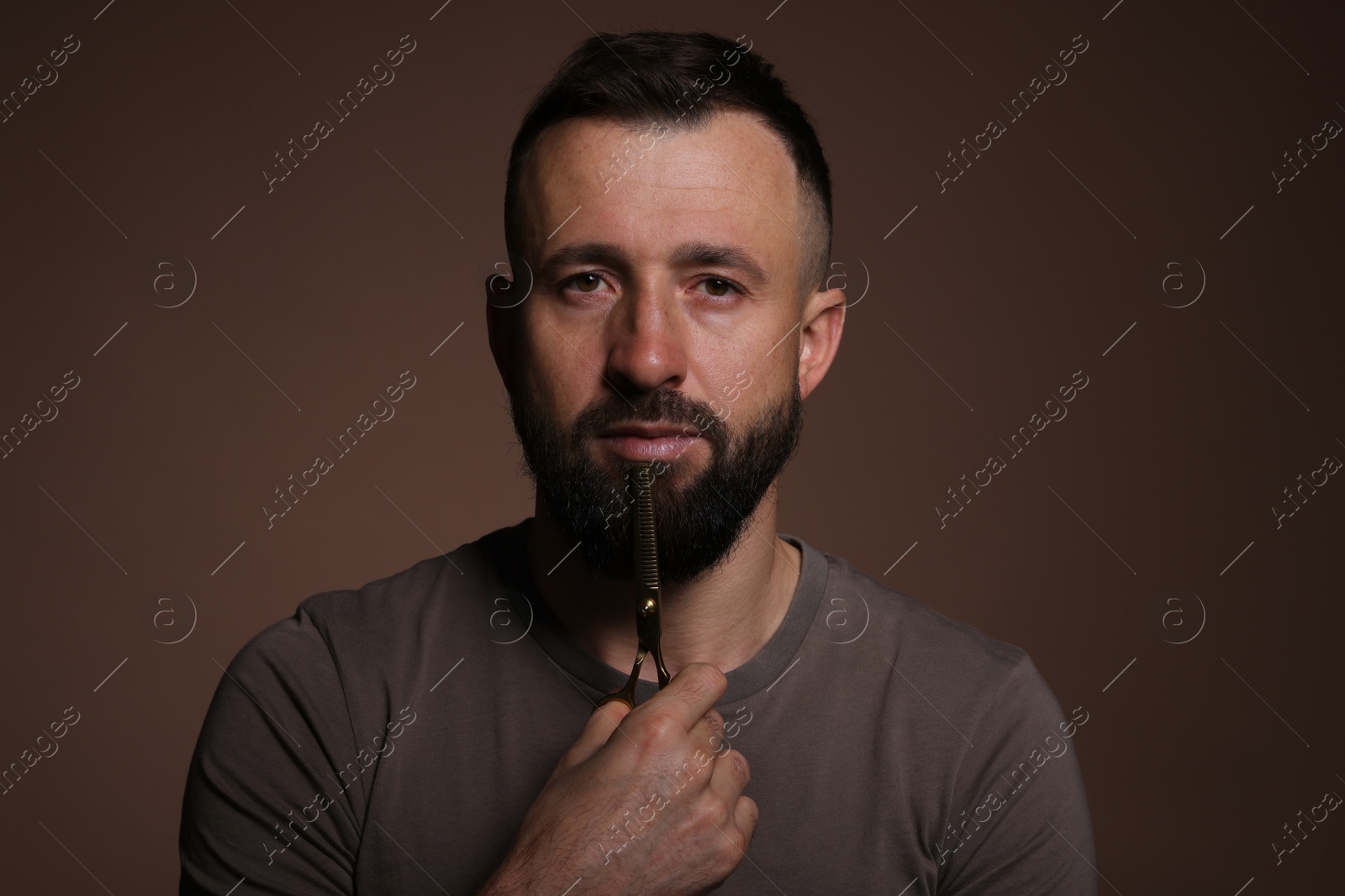 Photo of Bearded man holding scissors on brown background