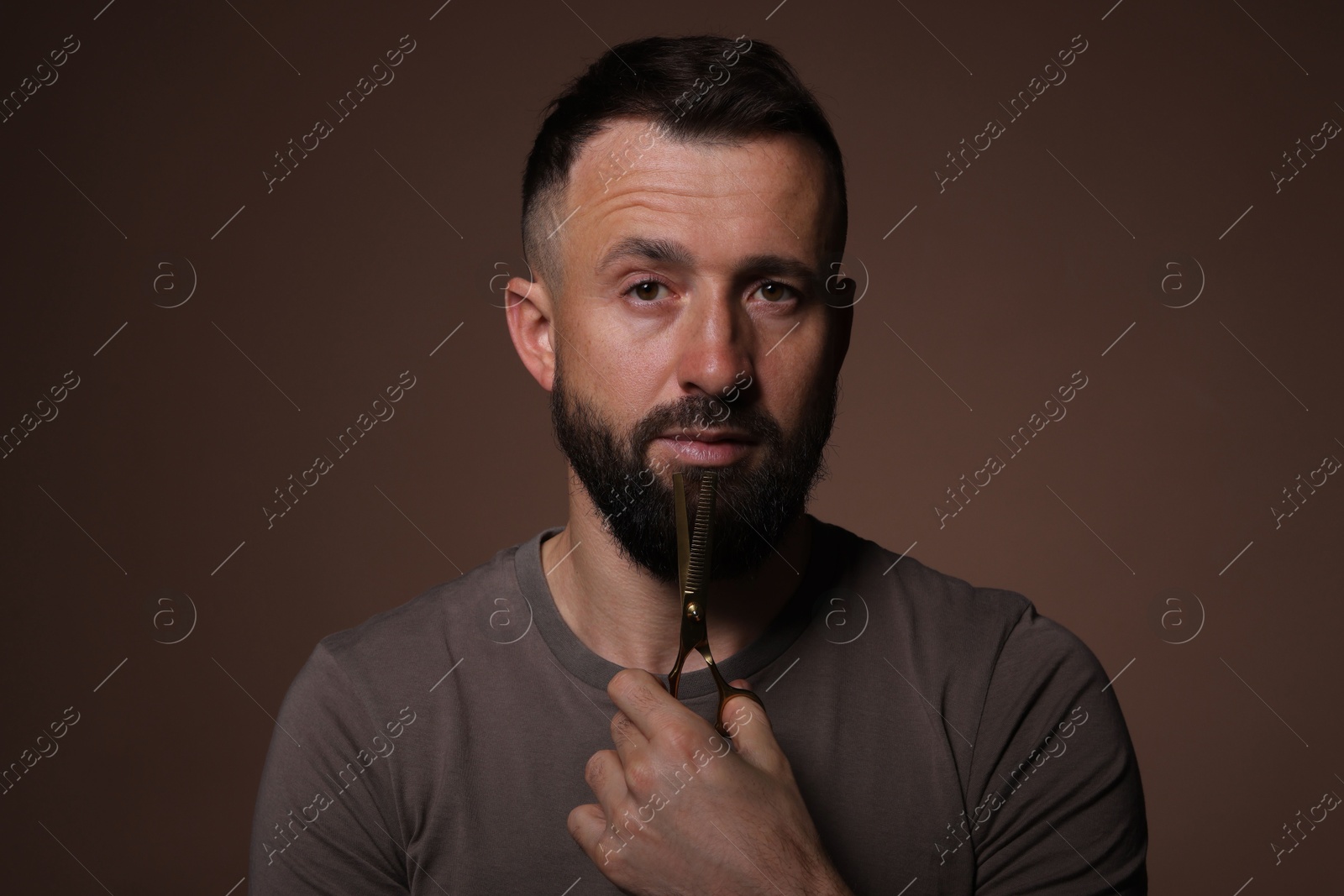 Photo of Bearded man holding scissors on brown background