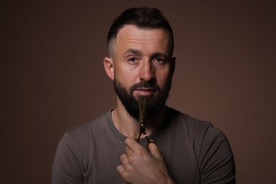 Photo of Bearded man holding scissors on brown background