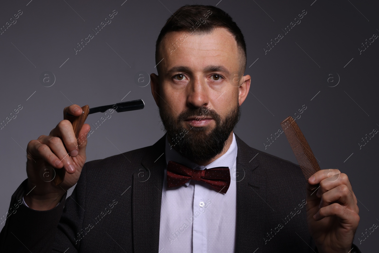 Photo of Bearded man holding blade and scissors on grey background