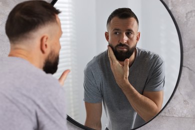 Photo of Handsome bearded man near mirror in bathroom