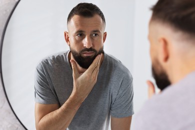 Photo of Handsome bearded man near mirror in bathroom