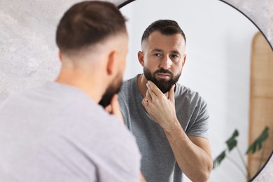 Photo of Handsome bearded man near mirror in bathroom