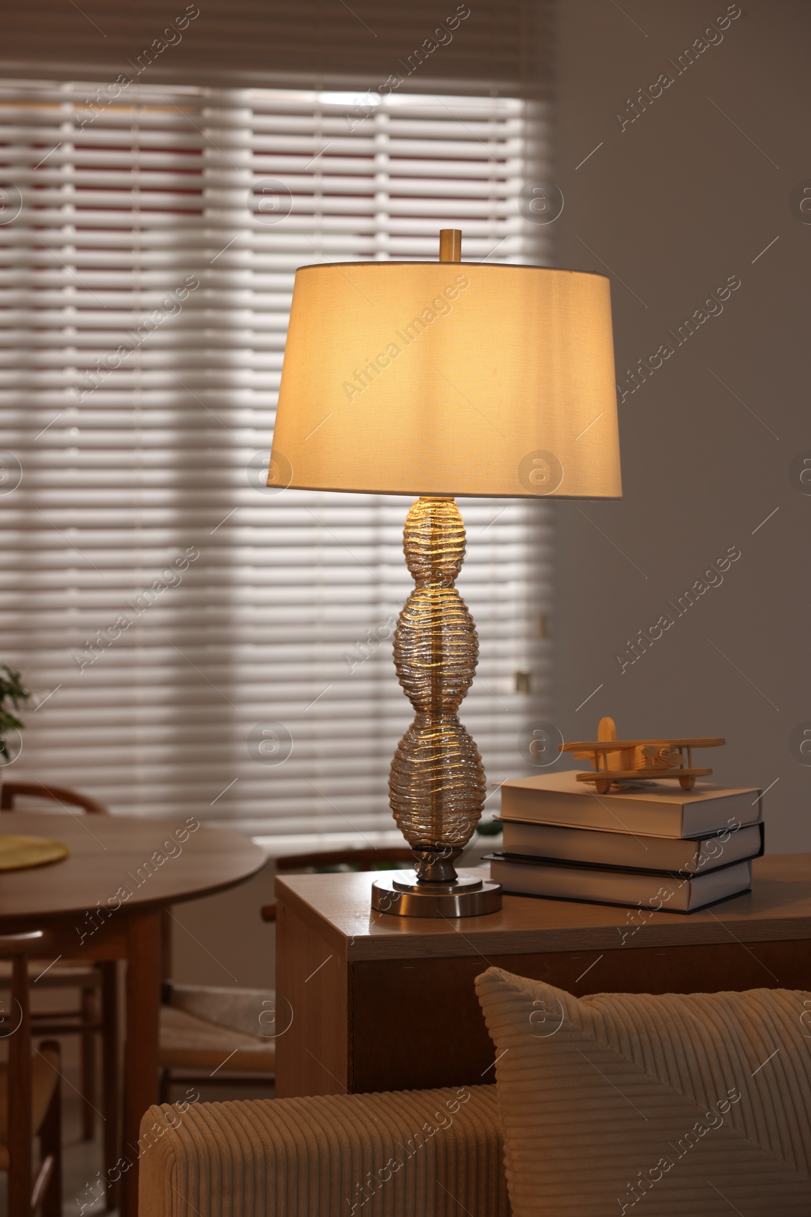 Photo of Beautiful night lamp, stack of books and airplane model on chest of drawers indoors