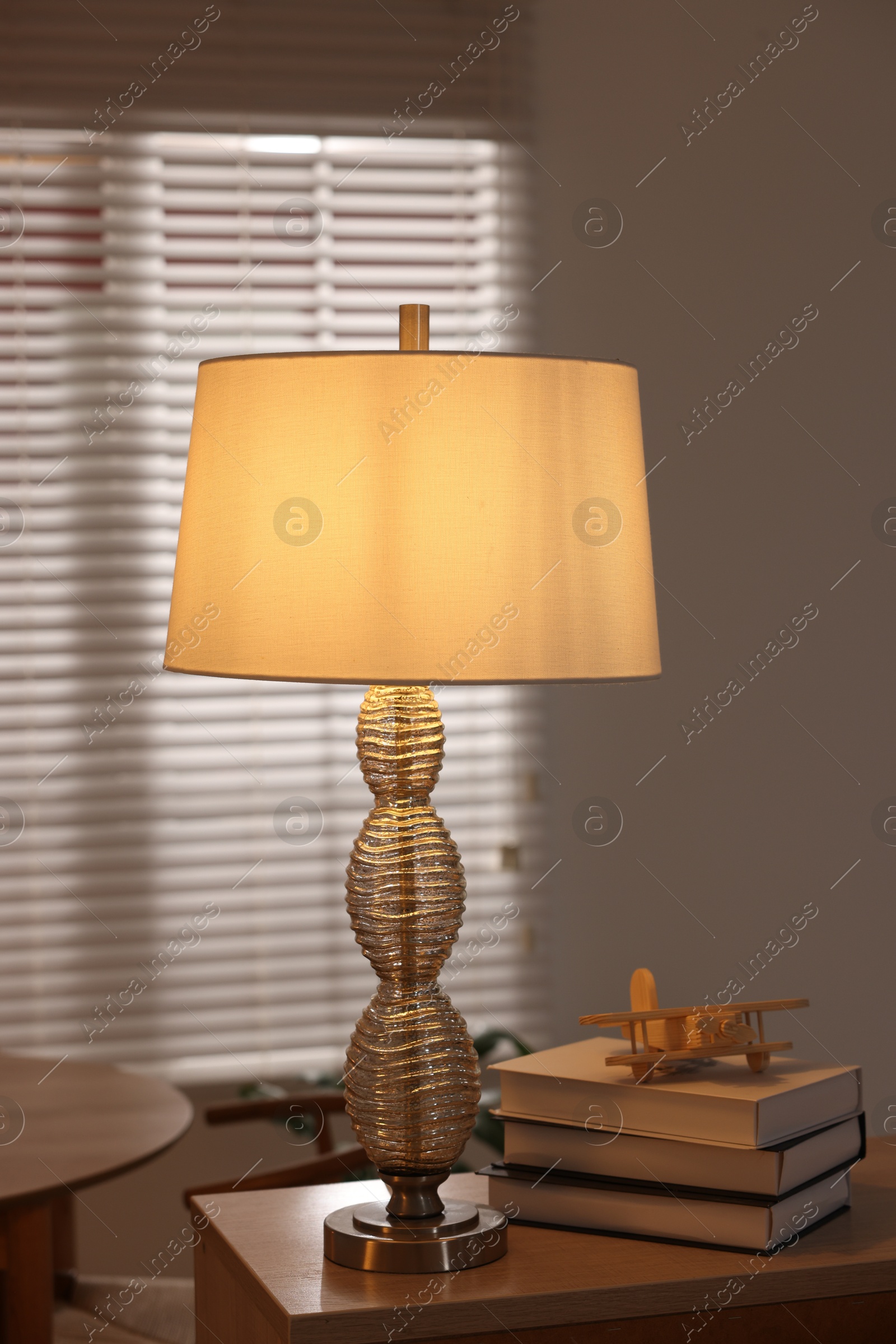 Photo of Beautiful night lamp, stack of books and airplane model on chest of drawers indoors