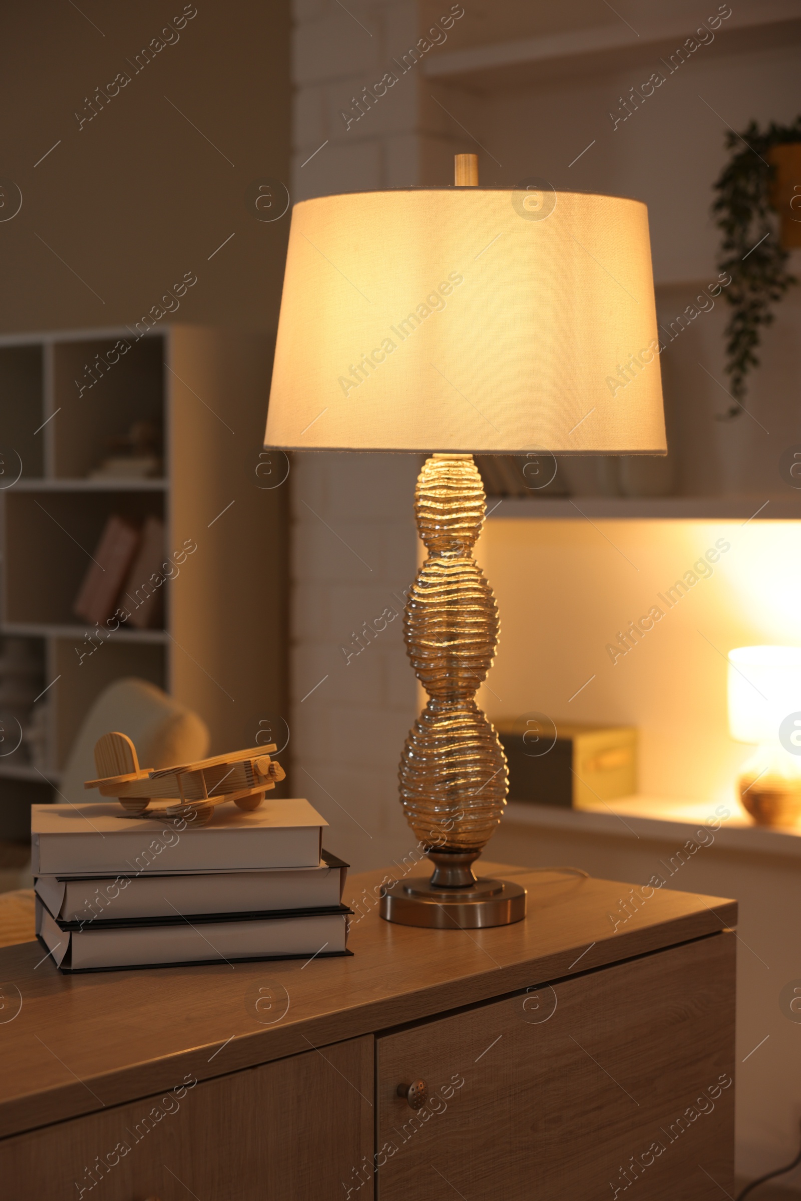 Photo of Beautiful night lamp, stack of books and airplane model on chest of drawers indoors