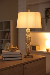 Photo of Beautiful night lamp, stack of books and airplane model on chest of drawers indoors