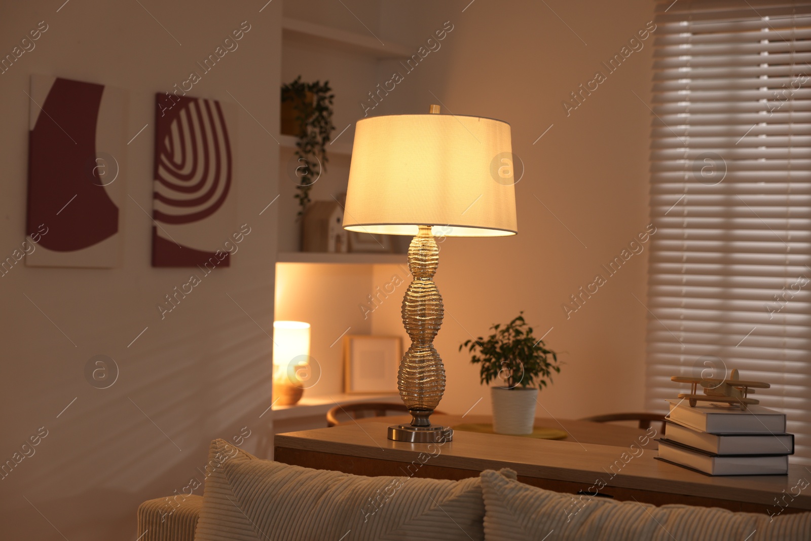 Photo of Beautiful night lamp, stack of books and airplane model on chest of drawers indoors