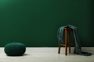 Photo of Stylish knitted pouf and wooden stool with blanket near green wall indoors, space for text