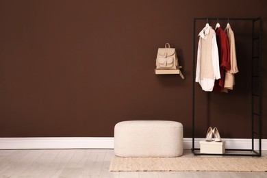 Photo of Stylish ottoman and rack with clothes in hallway. Space for text