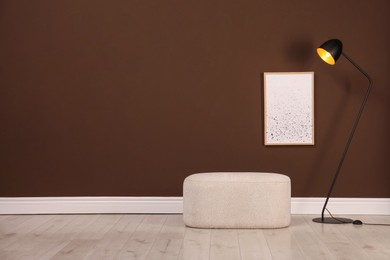 Photo of Stylish ottoman and lamp near brown wall in room. Space for text