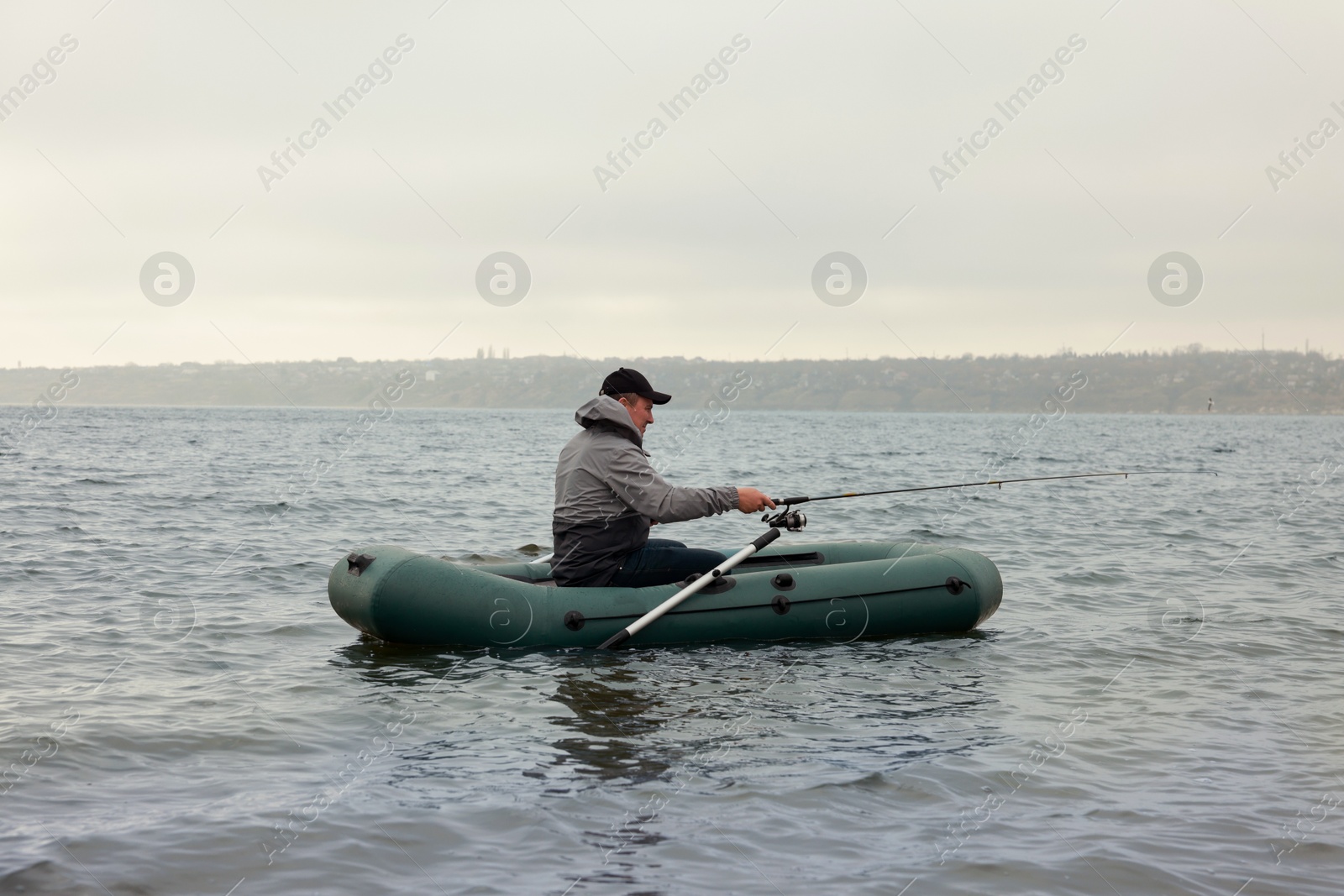 Photo of Man fishing with rod from inflatable rubber boat on river