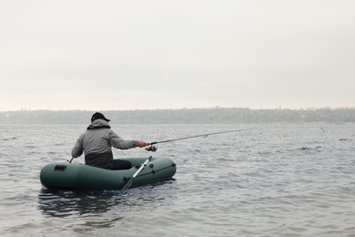 Photo of Man fishing with rod from inflatable rubber boat on river, back view