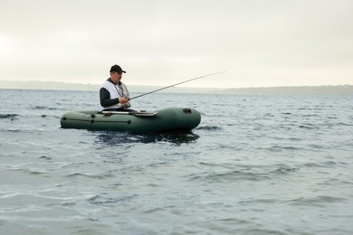 Photo of Man fishing with rod from inflatable rubber boat on river