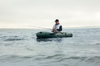 Photo of Man fishing with rod from inflatable rubber boat on river