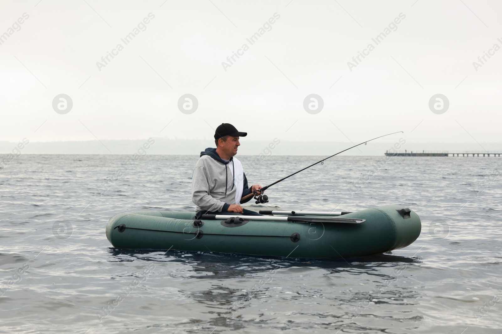 Photo of Man fishing with rod from inflatable rubber boat on river