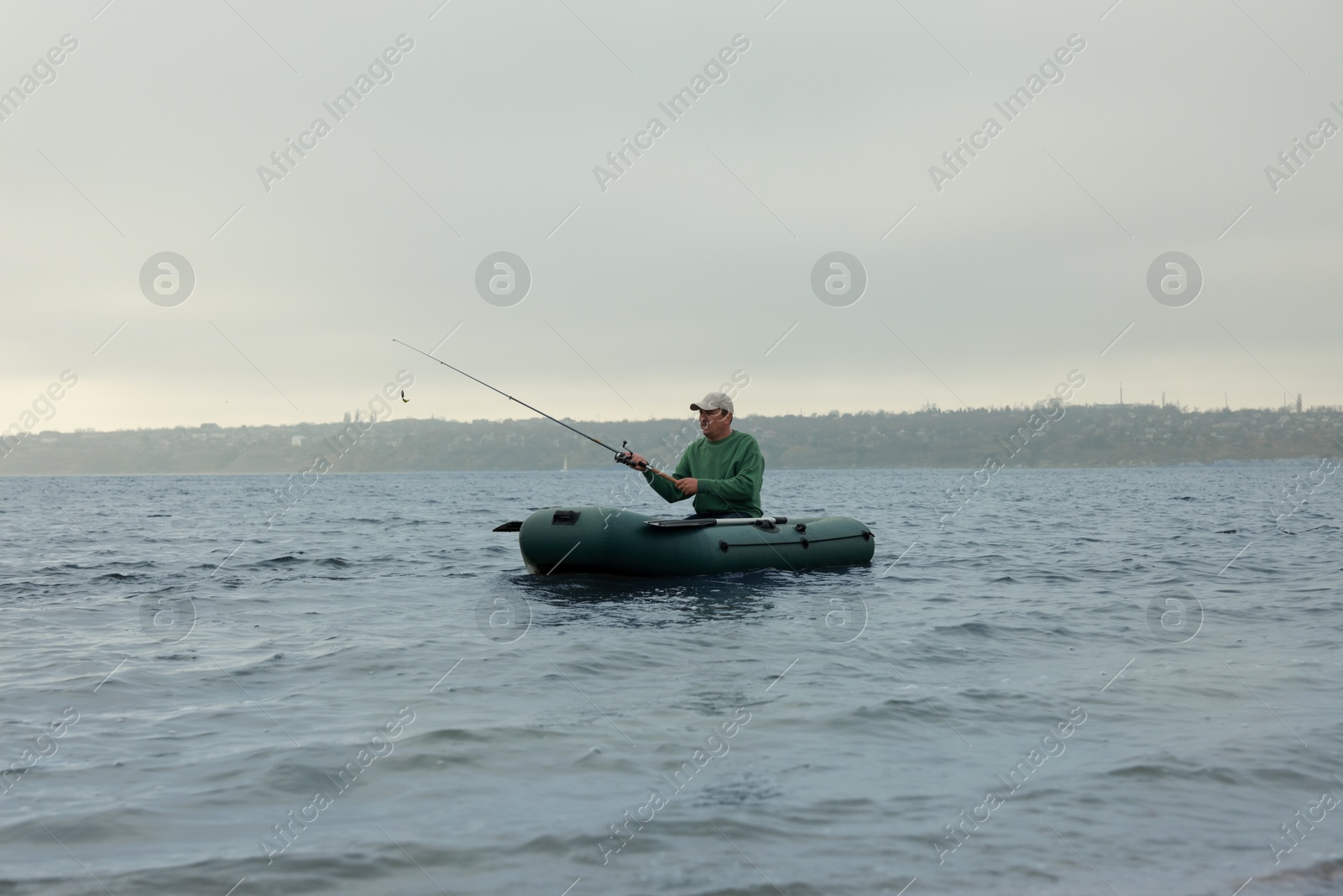 Photo of Man fishing with rod from inflatable rubber boat on river