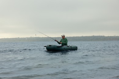 Photo of Man fishing with rod from inflatable rubber boat on river