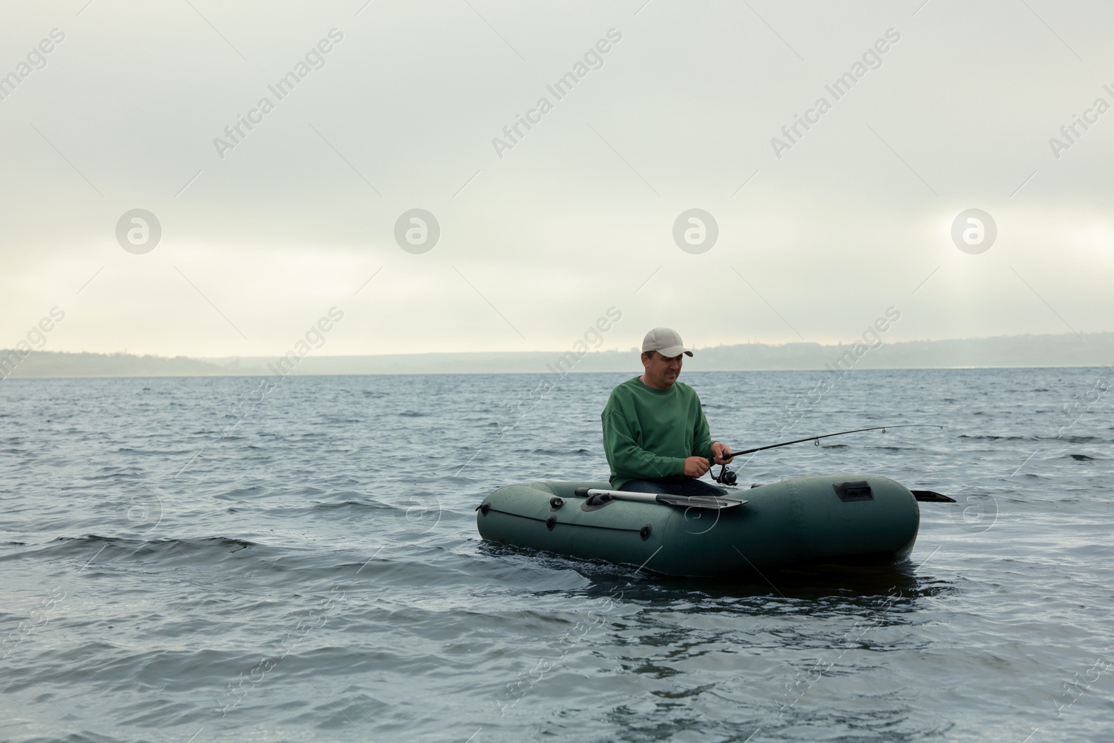 Photo of Man fishing with rod from inflatable rubber boat on river