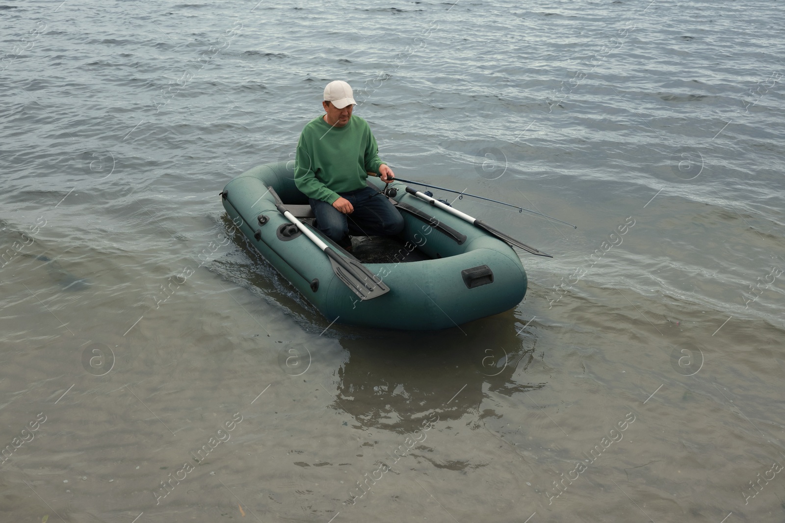 Photo of Man fishing with rod from inflatable rubber boat on river