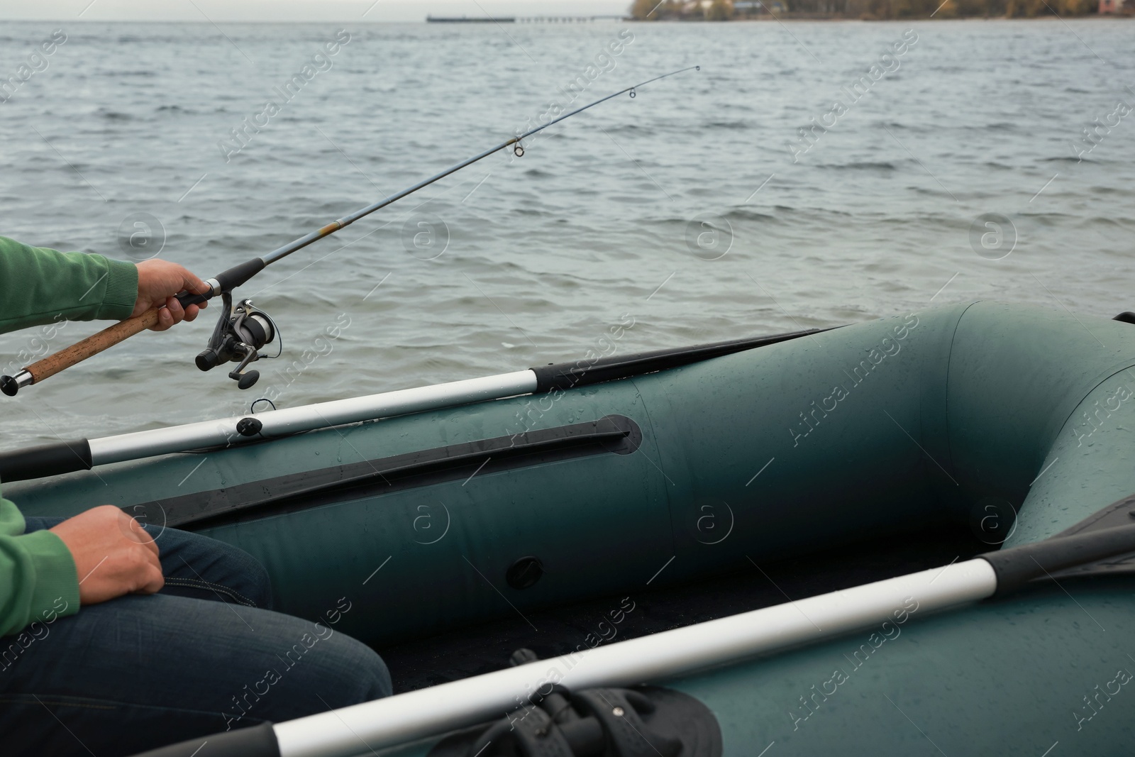 Photo of Man fishing with rod from inflatable rubber boat on river, closeup