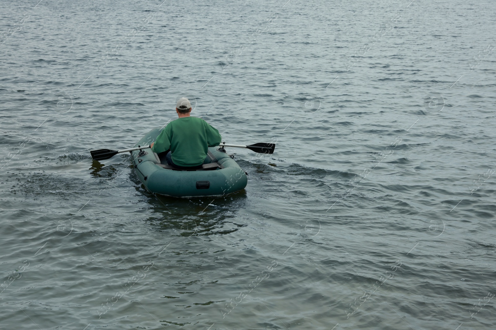 Photo of Fisherman rowing inflatable rubber boat on river, back view