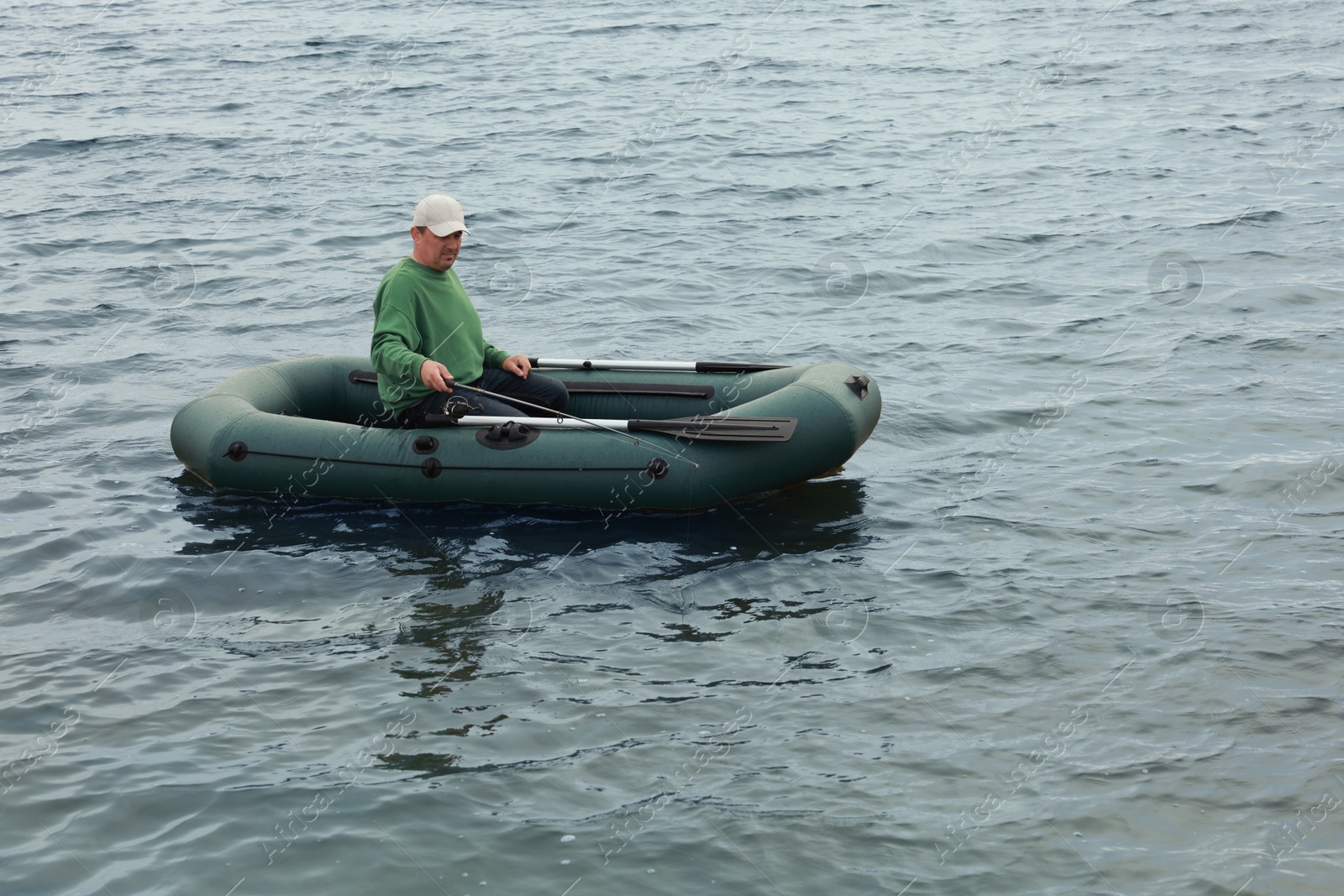 Photo of Man fishing with rod from inflatable rubber boat on river