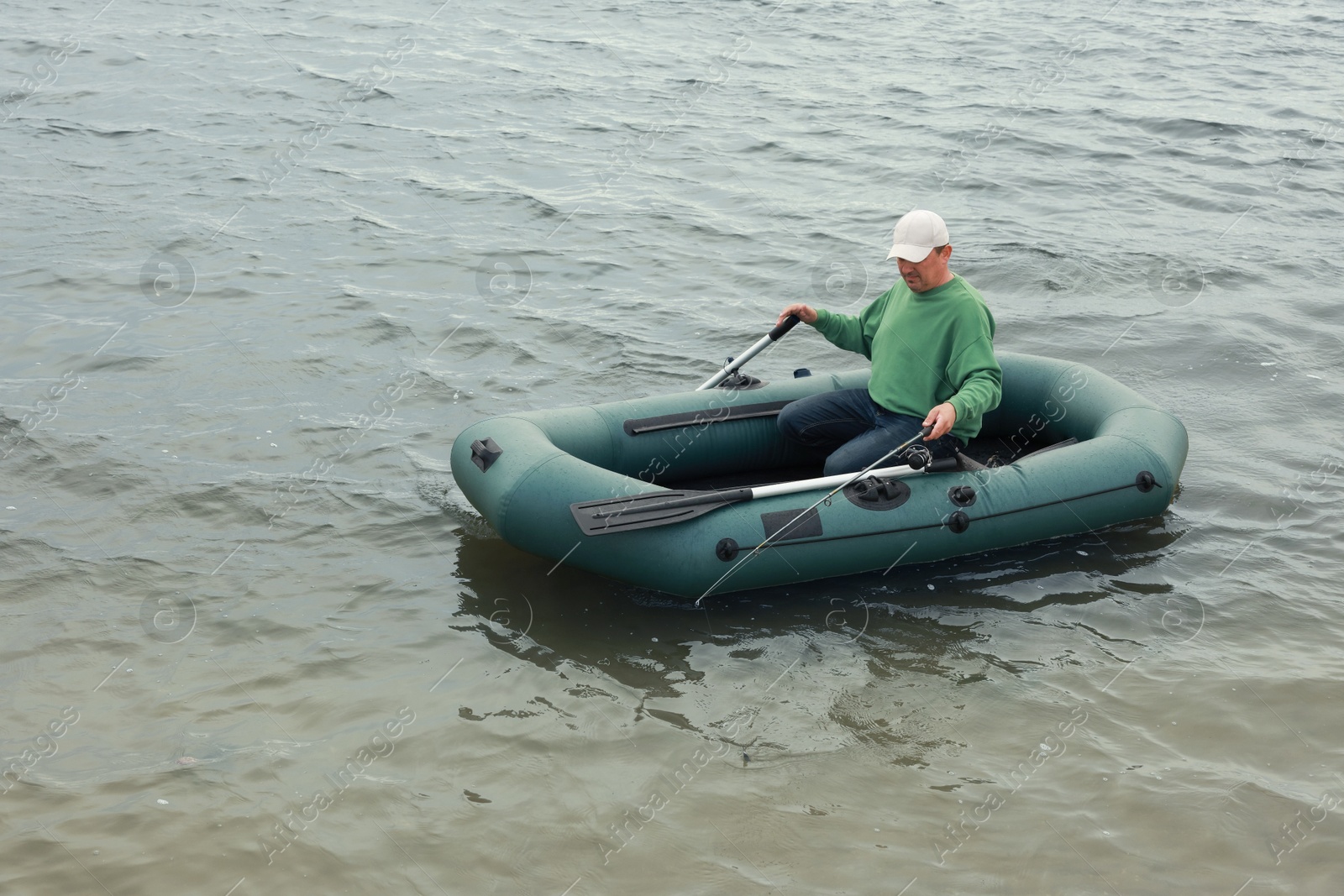 Photo of Man fishing with rod from inflatable rubber boat on river