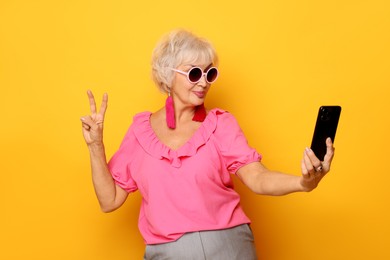 Cool grandmother showing V-sign while taking selfie on orange background