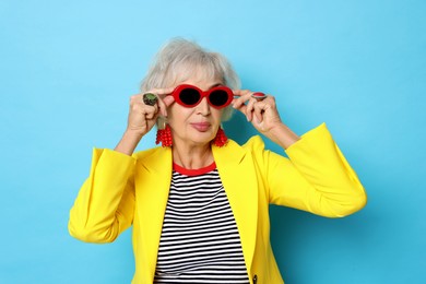 Photo of Portrait of fashionable grandmother in sunglasses and yellow jacket on light blue background