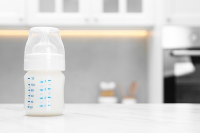 Photo of Feeding bottle with milk on white table indoors. Space for text