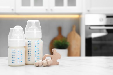 Photo of Feeding bottles with milk and toy on white table indoors. Space for text