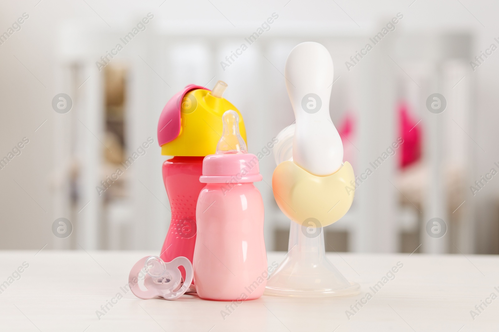 Photo of Feeding bottles with milk, breast pump and pacifier on white table indoors