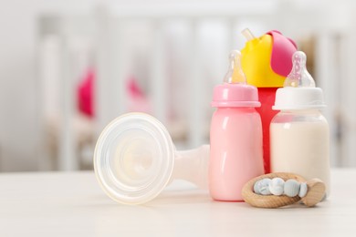 Photo of Feeding bottles with milk, breast pump and teether on white table indoors