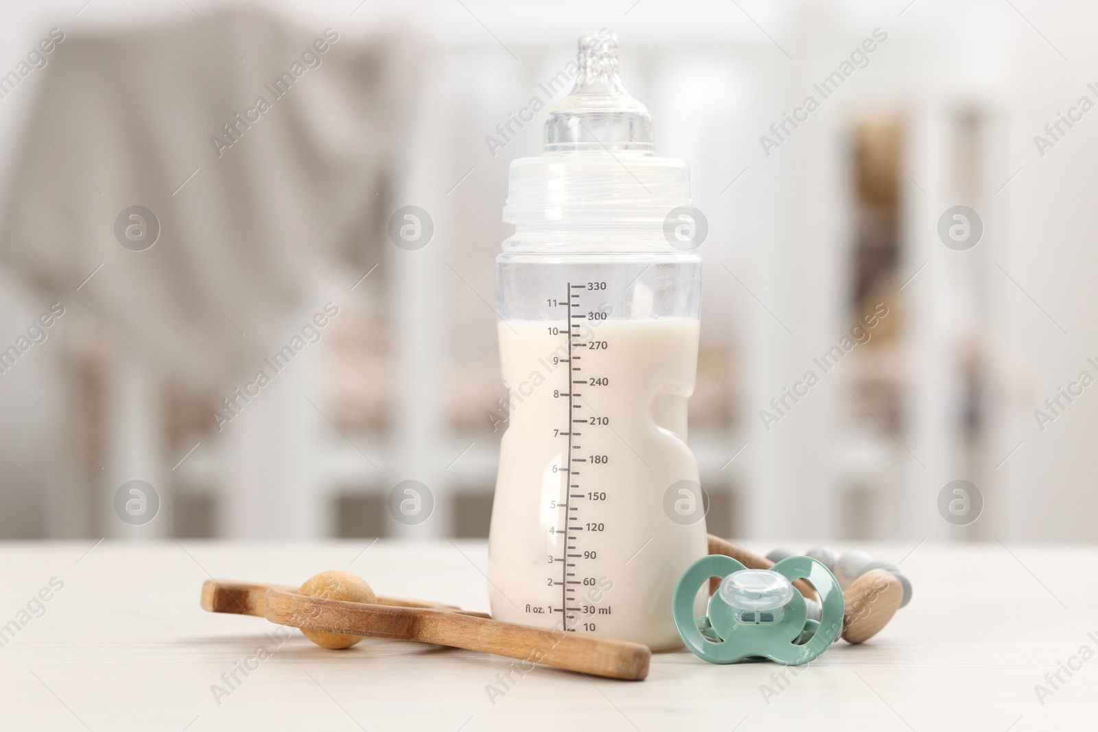 Photo of Feeding bottle with baby formula, pacifier and toys on white table indoors