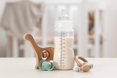 Photo of Feeding bottle with baby formula, pacifier and toys on white table indoors