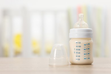 Photo of Feeding bottle with baby formula on wooden table indoors. Space for text